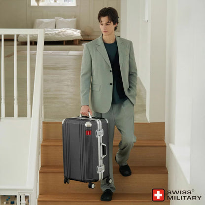 Angle view of the silver and dark grey Swiss Military 63.5cm hardside suitcase showing its aluminium edge frame and double urethane wheels on a light surface.