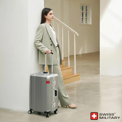 Angle view of the silver and dark grey Swiss Military 63.5cm hardside suitcase showing its aluminium edge frame and double urethane wheels on a light surface.