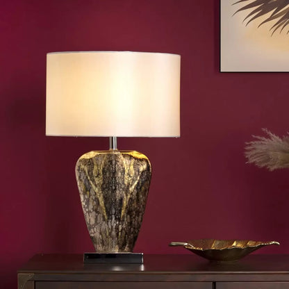A close-up profile shot of the Syracuse table lamp showcasing its reflective, antique silver-and-gold mercury glass base and textured cream faux silk shade set against a neutral, wood-paneled wall.