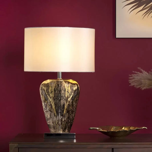 A close-up profile shot of the Syracuse table lamp showcasing its reflective, antique silver-and-gold mercury glass base and textured cream faux silk shade set against a neutral, wood-paneled wall.