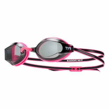 Three pairs of low-profile TYR junior swimming goggles in blue, pink, and clear silicone frames resting on a damp pool bench, showing the anti-fog coated polycarbonate lenses.