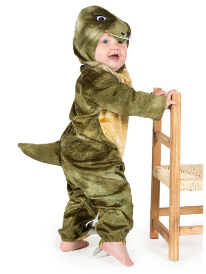 Baby wearing a soft green T Rex jumpsuit costume with a plush dinosaur headpiece in a cozy play area.
