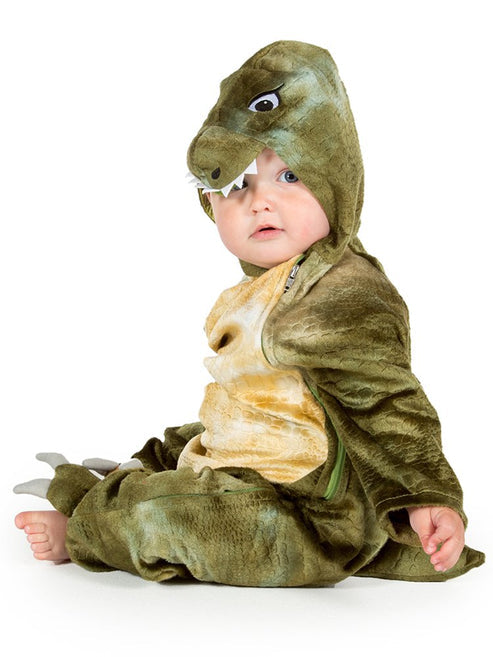 Baby wearing a soft green T Rex jumpsuit costume with a plush dinosaur headpiece in a cozy play area.