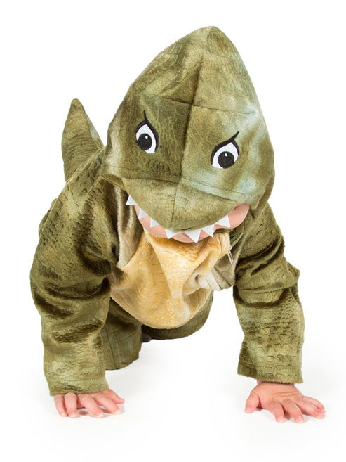 Baby wearing a soft green T Rex jumpsuit costume with a plush dinosaur headpiece in a cozy play area.