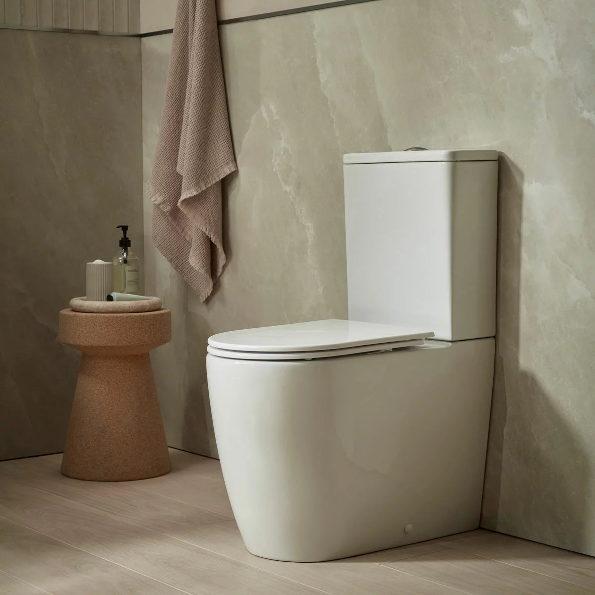 Side profile of the white ceramic Tavistock Curve closed back toilet installed against a dark slate bathroom wall, showcasing its smooth rimless bowl and ultra-slim soft-close seat.