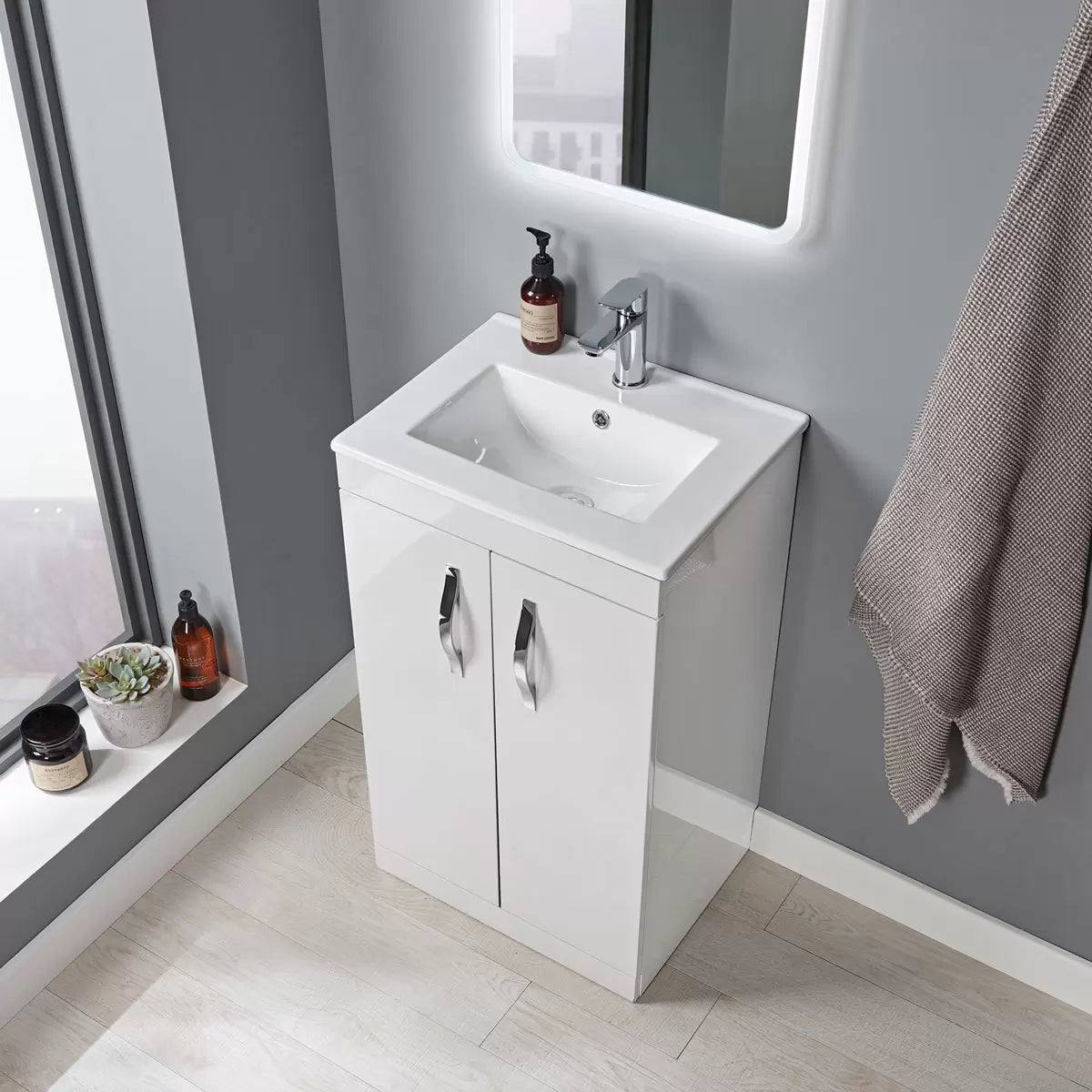 Front angle view of the Tavistock Vesta gloss white 51cm floor mounted vanity unit with integrated white ceramic basin and sleek chrome handles in a modern tiled bathroom setting.