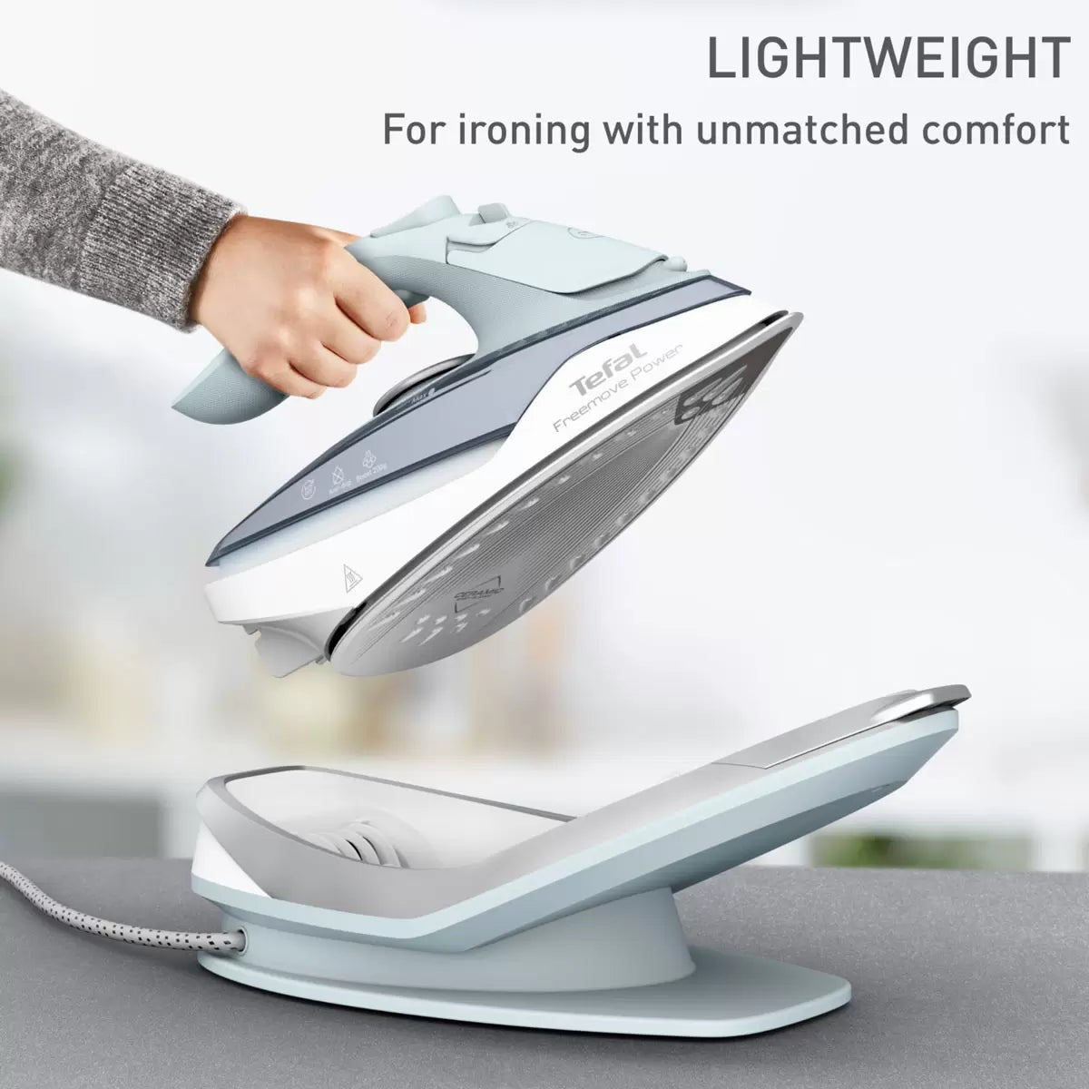 Tefal Freemove Power cordless steam iron FV6642G0 resting on its horizontal charging base with lock system on an ironing board.