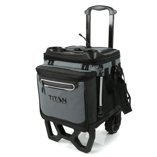 Side angle view of the dark grey Titan 22.5L 60 can cooler mounted securely onto its folded out black all-terrain cart with oversized rugged wheels, set on a gravel path.