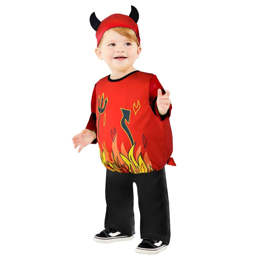 Front view of a toddler wearing a red cute devil Halloween costume with attached soft horns and tail in a festive living room setting.