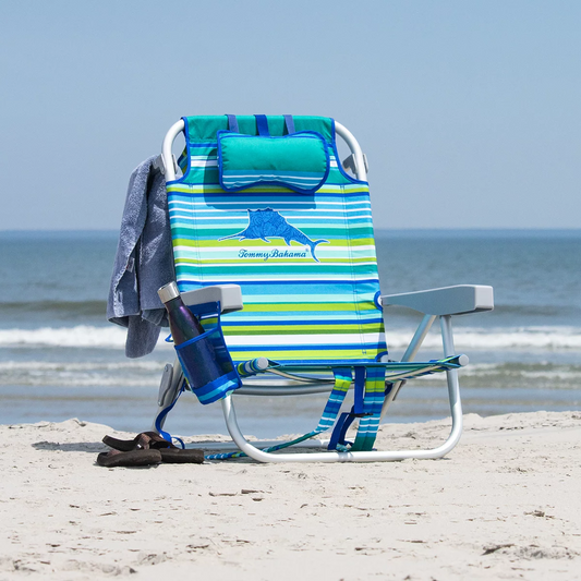 Lightweight blue woven polyester Tommy Bahama backpack beach chair with padded shoulder straps, drink holder, and integrated rear cooler pouch unfolded on a sandy beach.