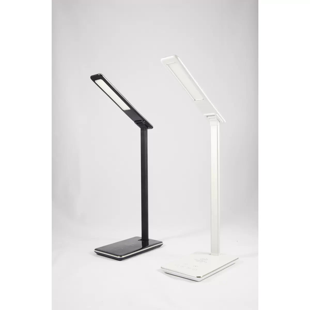 A close-up angle of the matte finish TouchDown LED lamp, showcasing a smartphone charging on its integrated wireless base beside a stack of books on a wooden bedside table.