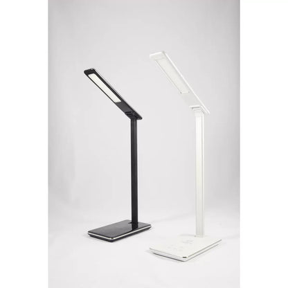 A close-up angle of the matte finish TouchDown LED lamp, showcasing a smartphone charging on its integrated wireless base beside a stack of books on a wooden bedside table.