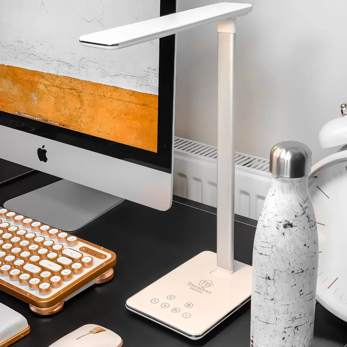 A close-up angle of the matte finish TouchDown LED lamp, showcasing a smartphone charging on its integrated wireless base beside a stack of books on a wooden bedside table.