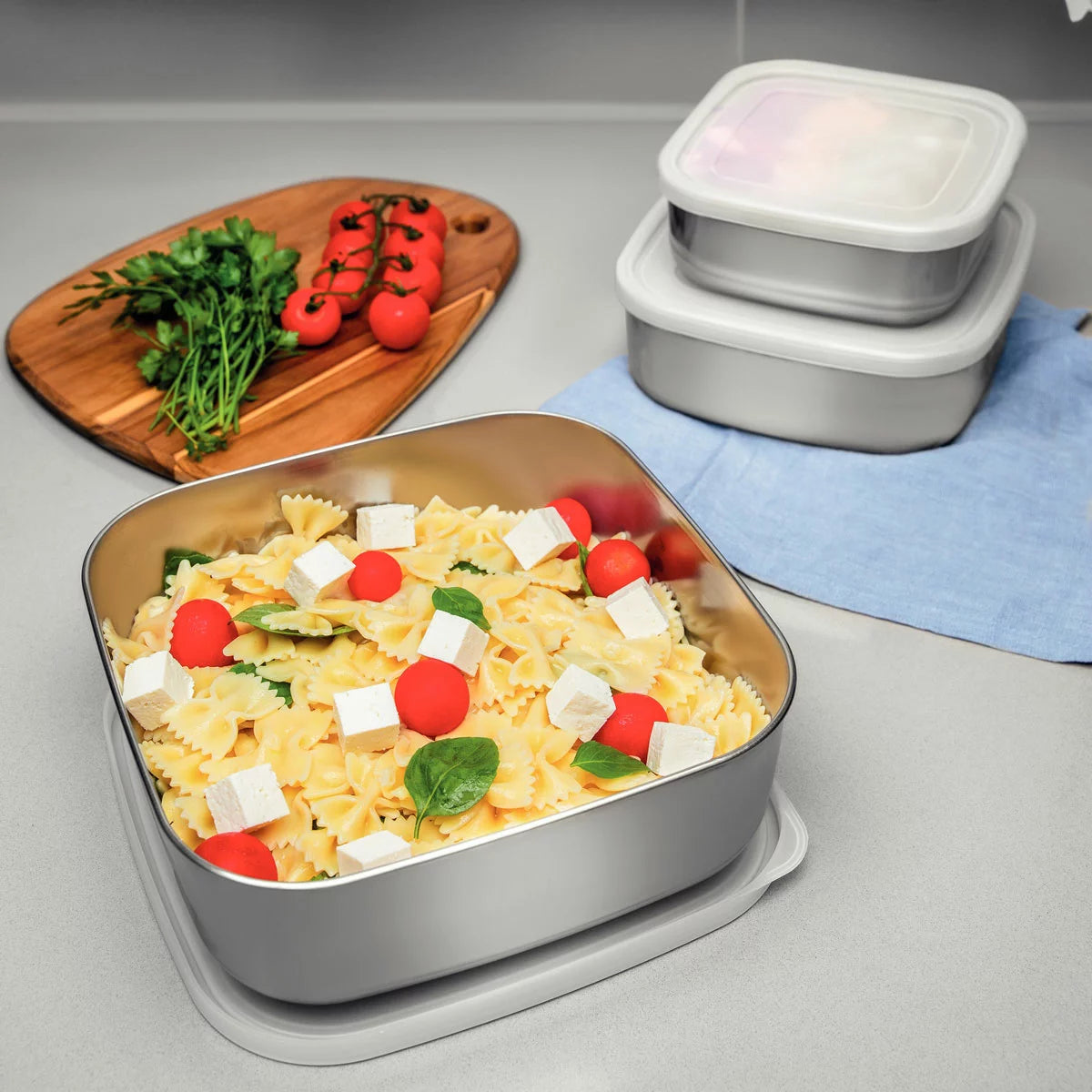Tramontina 3-piece stainless steel food storage container set with airtight lids on a kitchen counter.