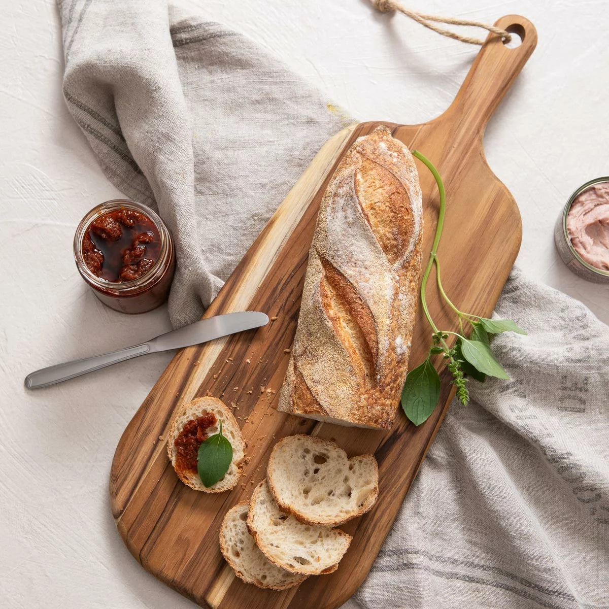Two rich golden-brown Tramontina teak cutting boards of different sizes resting flat on a modern, brightly lit kitchen countertop.