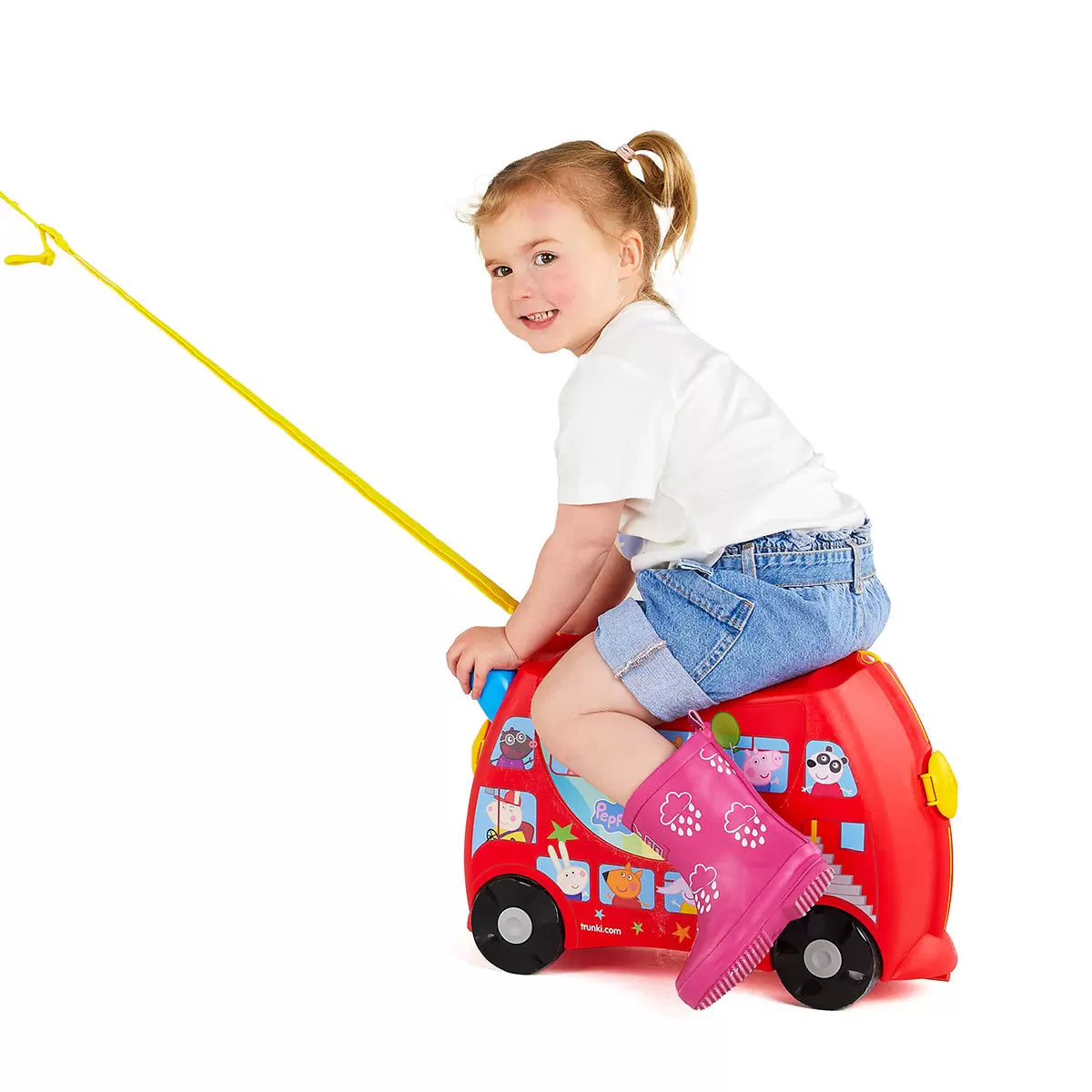 The Trunki Peppa Pig Party Bus ride-on suitcase in bright red with Peppa Pig branding, displayed on a clean studio floor to show its wheels and steering horns.