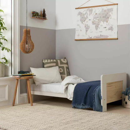 Front angle of the Tutti Bambini Alba Cot Bed in White Sand and Distressed Oak finish showing the included sprung mattress inside a brightly lit nursery setting.