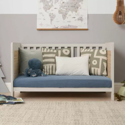 Front angle of the Tutti Bambini Alba Cot Bed in White Sand and Distressed Oak finish showing the included sprung mattress inside a brightly lit nursery setting.