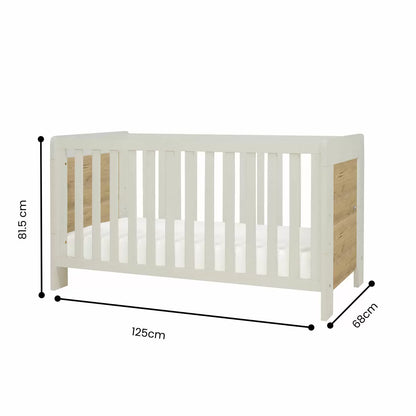 Three-quarter studio shot of the built white sand and distressed oak Tutti Bambini Alba Mini Cot Bed containing its fabric mattress.