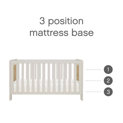 Three-quarter studio shot of the built white sand and distressed oak Tutti Bambini Alba Mini Cot Bed containing its fabric mattress.