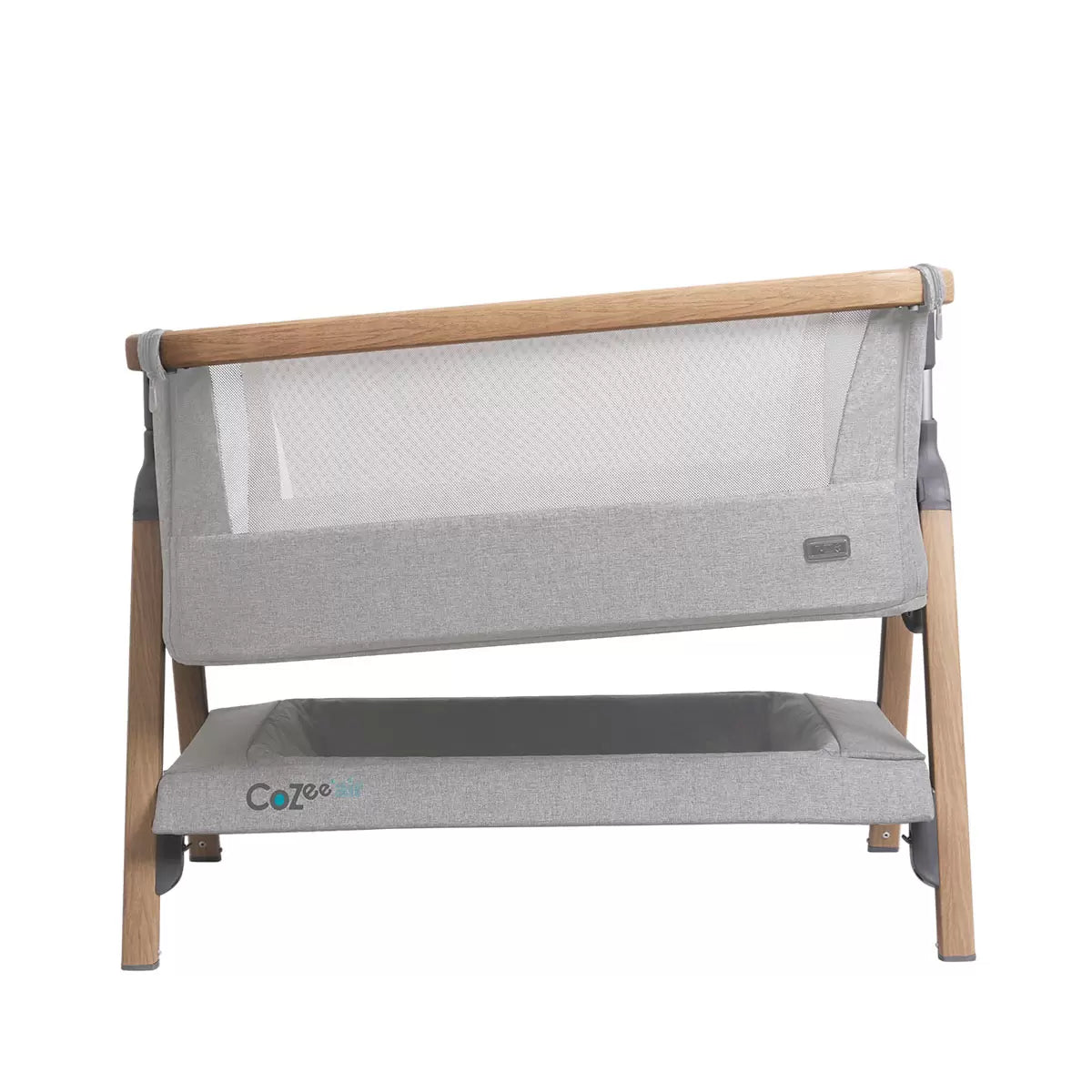 Side view of the Tutti Bambini CoZee Air bedside crib in oak and silver finish showing dual mesh windows, mattress, and detachable rocking arches inside a neutral nursery.