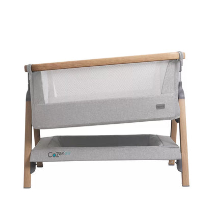 Side view of the Tutti Bambini CoZee Air bedside crib in oak and silver finish showing dual mesh windows, mattress, and detachable rocking arches inside a neutral nursery.