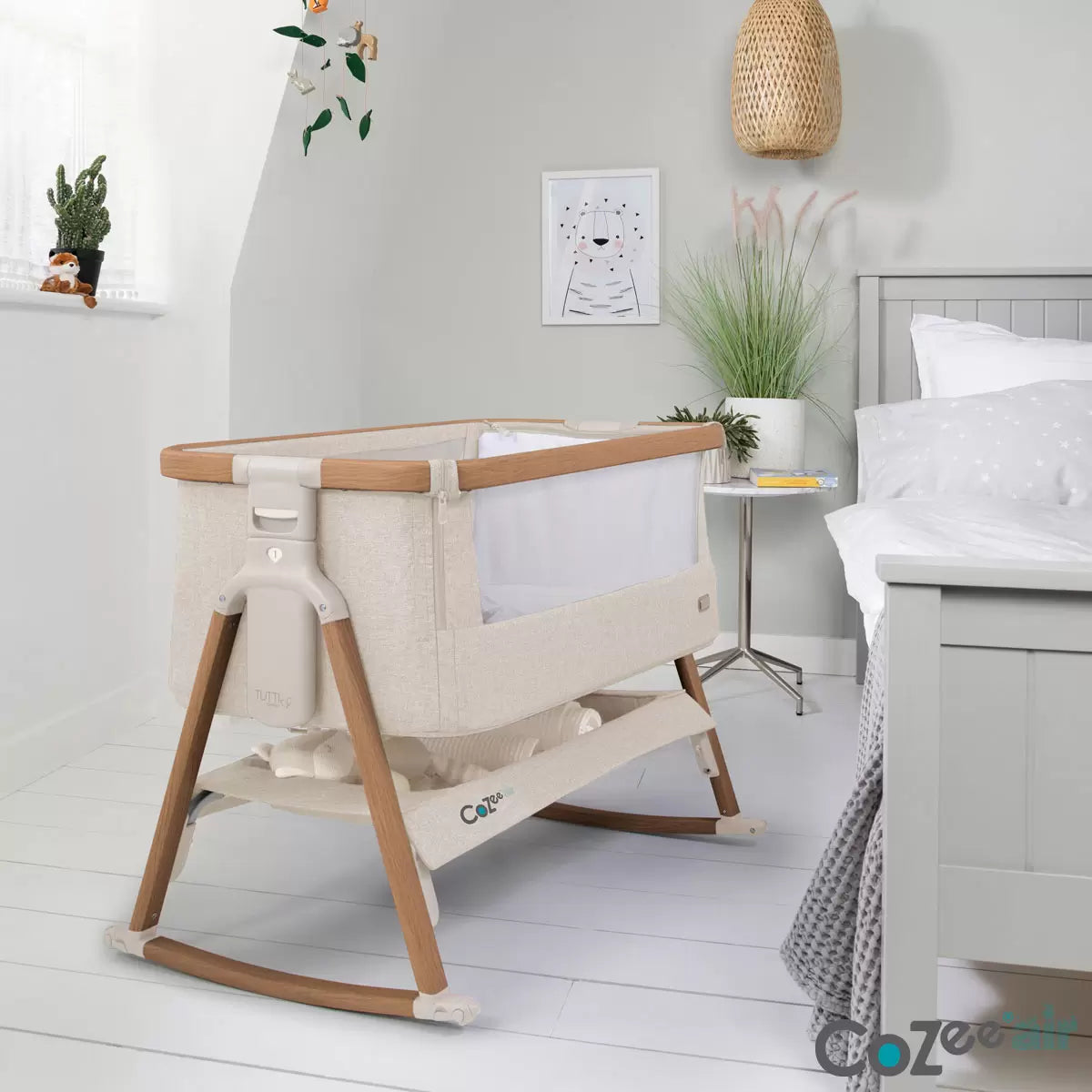 Tutti Bambini CoZee Air Bedside Rocking Crib in Walnut frame and Ecru fabric set up beside a adult bed with mesh side lowered.