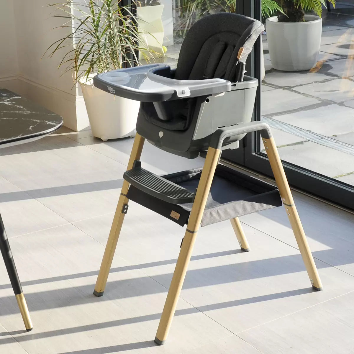A side profile of the Tutti Bambini Nova Evolutionary Highchair in grey, showcasing its modern frame design and adjustable tray in a bright kitchen environment.