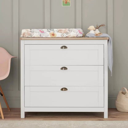 Front view of the white and oak Tutti Bambini Verona changing unit chest with three drawers and traditional brass handles shot in a brightly lit room.