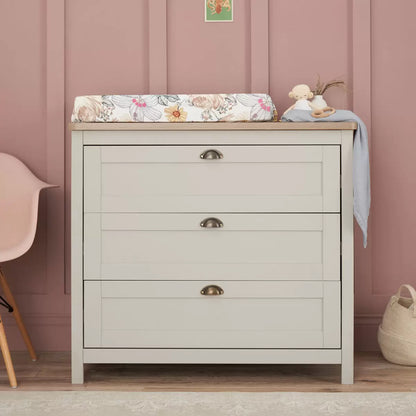 Front view of the grey and oak Tutti Bambini Verona changing unit featuring three closed drawers with traditional brass handles in a bright nursery setting.