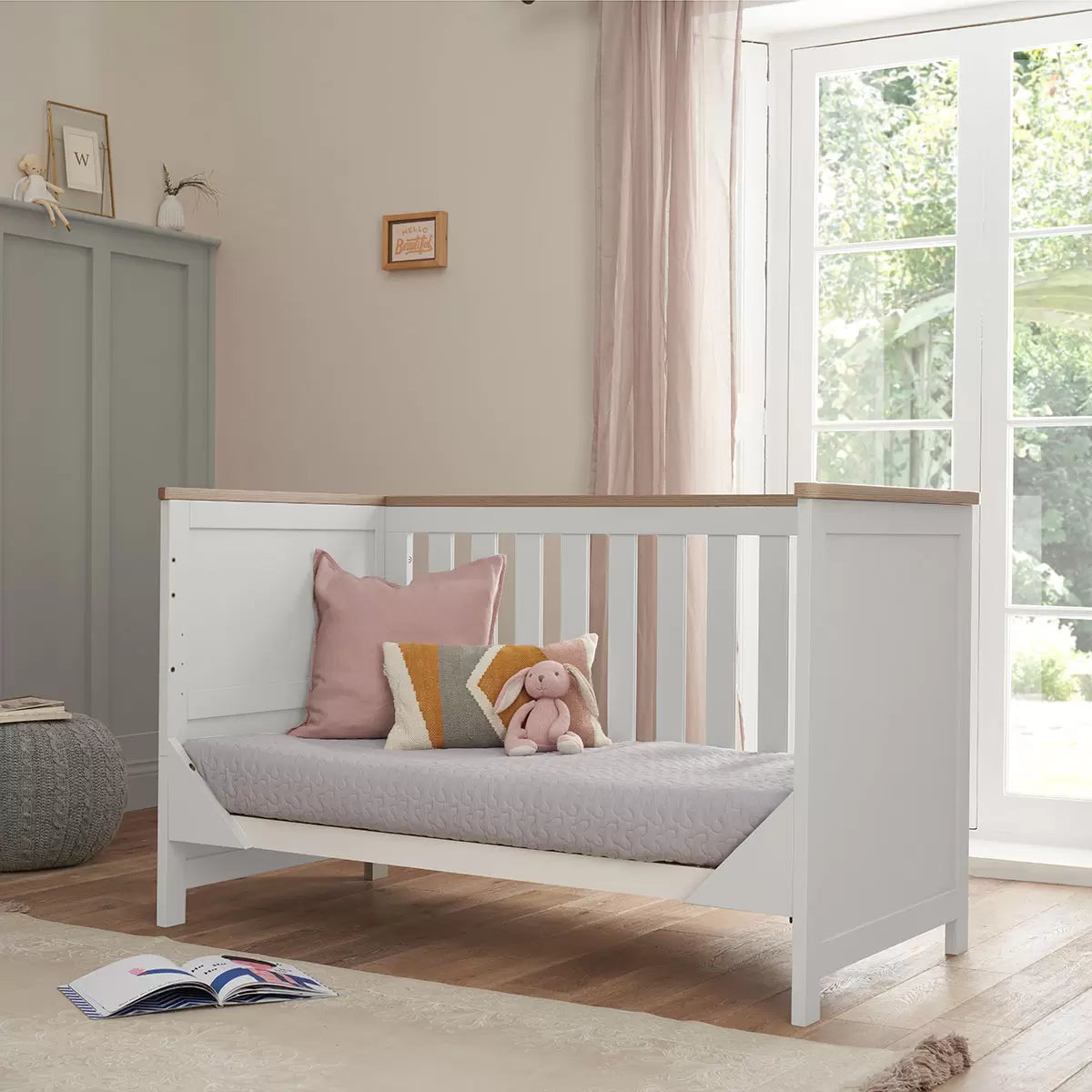 Three-quarter view of the built white and oak Tutti Bambini Verona cot bed showing the mattress inside a clean minimalist bedroom setting.