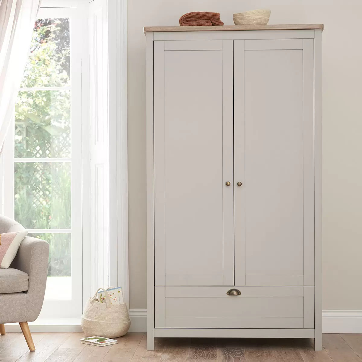 Front view of the Tutti Bambini Verona Wardrobe in soft-touch grey and oak finish with antique brass handles inside a modern nursery.