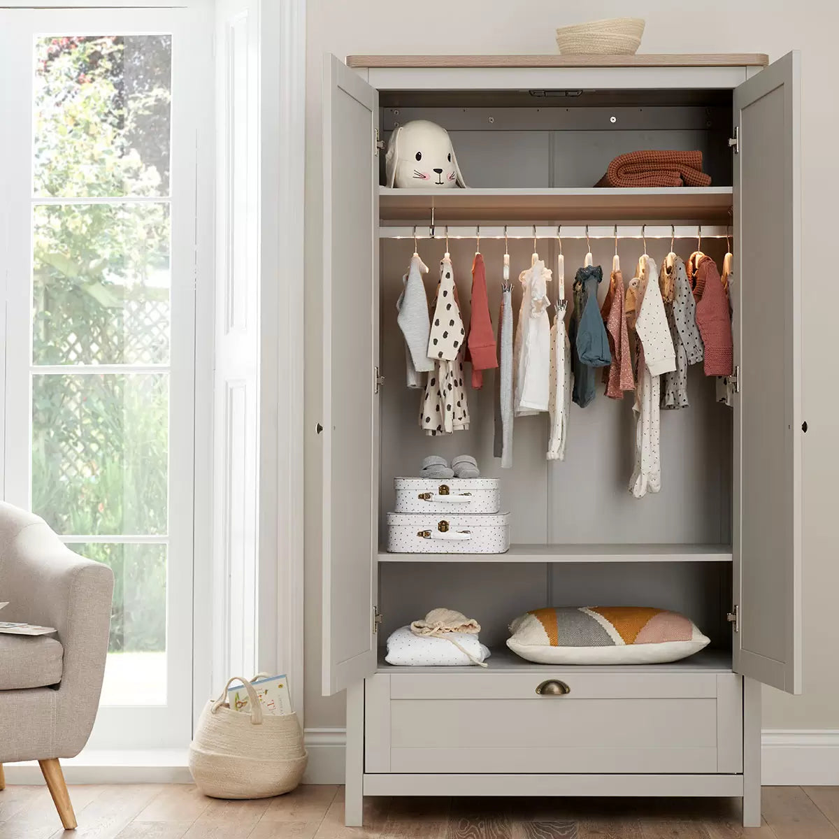 Front view of the Tutti Bambini Verona Wardrobe in soft-touch grey and oak finish with antique brass handles inside a modern nursery.