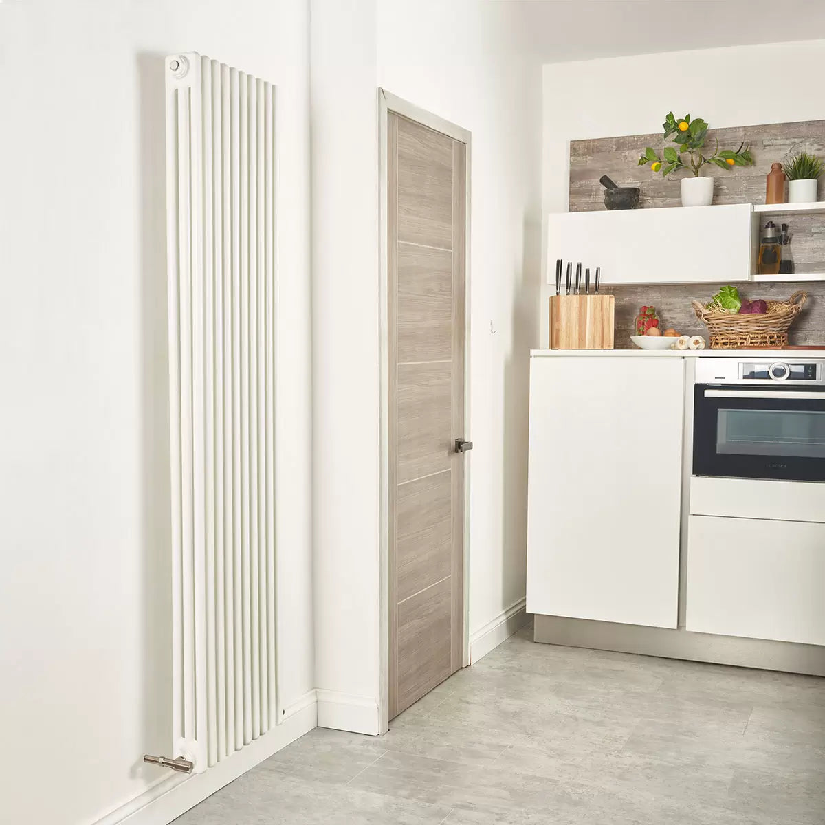 Vertical white 3-column steel radiator, 1800x465mm size, mounted on a light interior wall highlighting ten triple-tube sections.