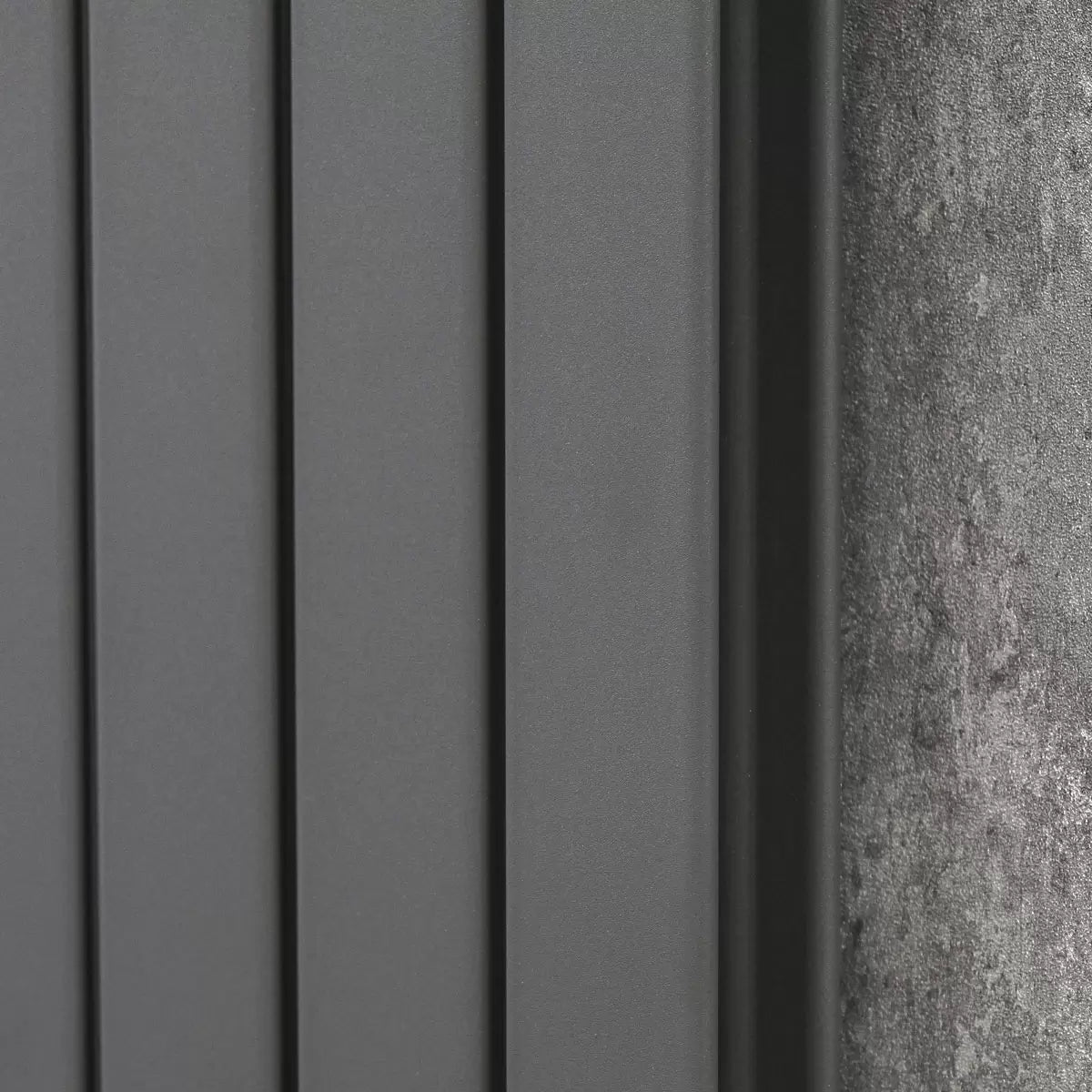 Vertical Ultraheat Tian Slate Grey tubular radiator mounted on a light gray wall in a modern open-plan living room setup.