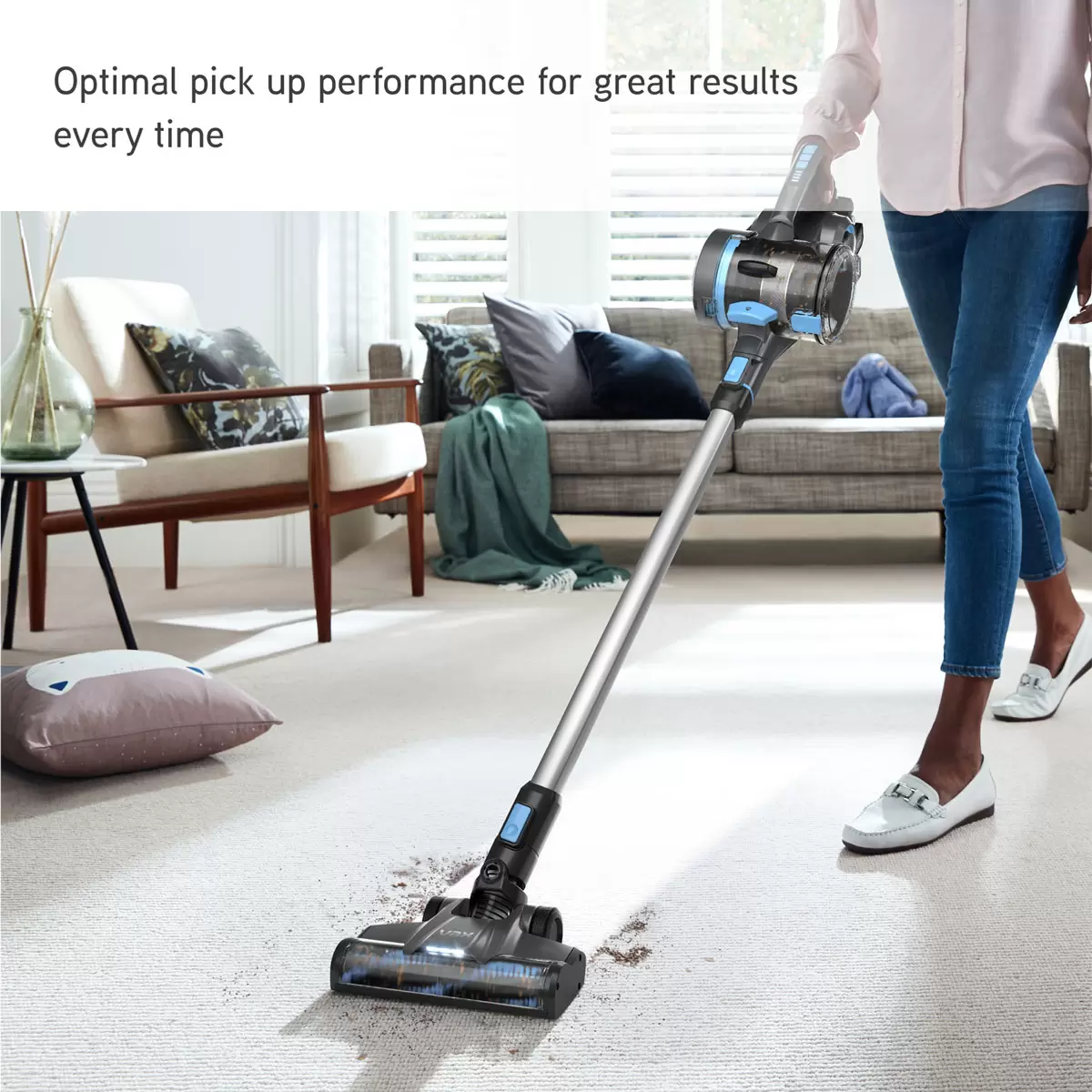 Metallic grey and blue VAX Blade 4 Classic Plus cordless stick vacuum CLSV-B4CA standing upright on a grey carpeted surface with its LED floorhead lit up.