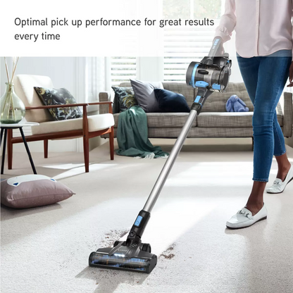 Metallic grey and blue VAX Blade 4 Classic Plus cordless stick vacuum CLSV-B4CA standing upright on a grey carpeted surface with its LED floorhead lit up.