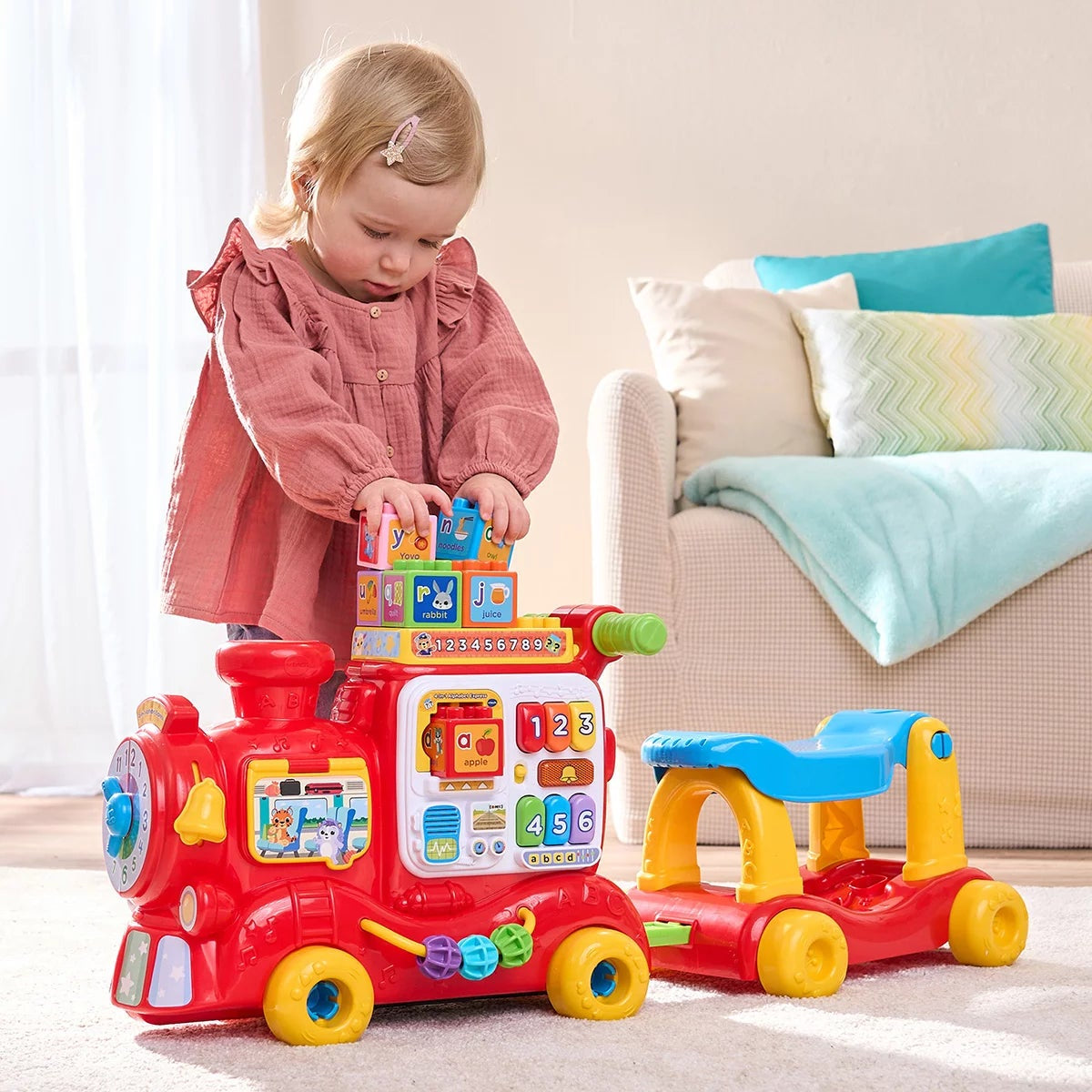 Side view of the bright red and yellow plastic VTech 4-in-1 Alphabet Express train showing the floor-play block reader, ride-on seat, and interactive light-up buttons on a plain white studio background.