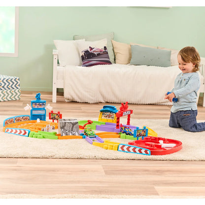 Brightly colored VTech Toot-Toot Drivers Super Circuit RC Raceway plastic track layout featuring a red RC car, motorized racer, tunnel, and remote control on a light wood floor.