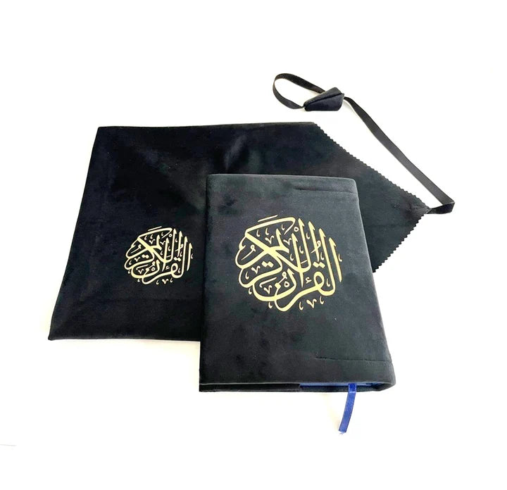 Angle view of a black soft velvet covered 13-line Quran with gold Arabic logo next to its matching velvet holder inside an open presentation gift box.