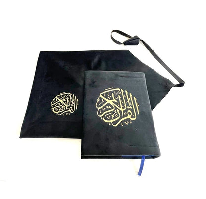 Angle view of a black soft velvet covered 13-line Quran with gold Arabic logo next to its matching velvet holder inside an open presentation gift box.