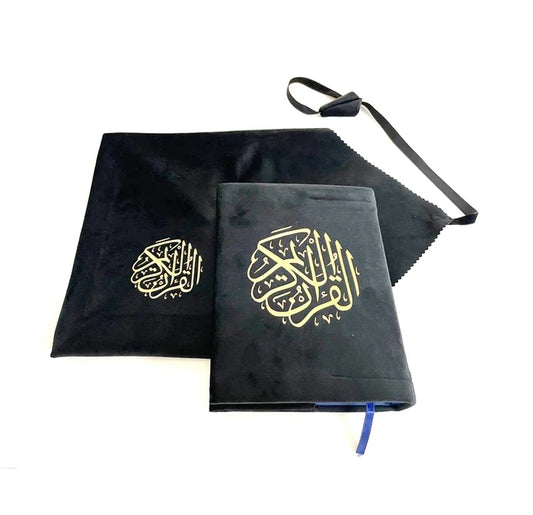 Angle view of a black soft velvet covered 13-line Quran with gold Arabic logo next to its matching velvet holder inside an open presentation gift box.