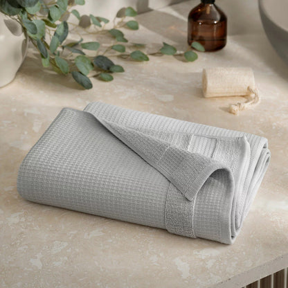 Close-up shot of the Welhome 100% cotton waffle-textured towel in grey, showing the terry backing on a modern bathroom wooden shelf.