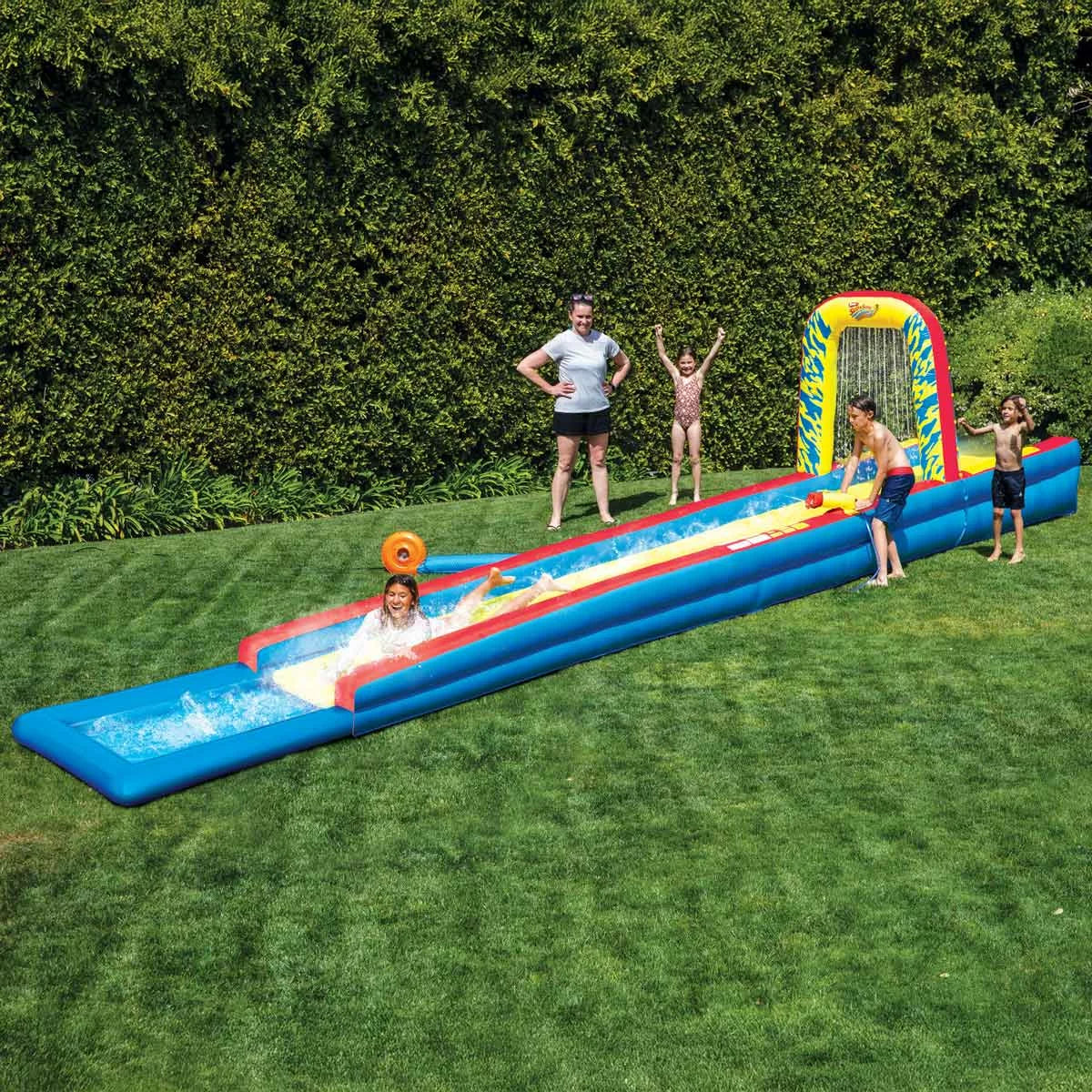 A giant 32-foot Wham-O inflatable Slip 'N Slide with blue and orange water lanes inflated in a grassy garden.