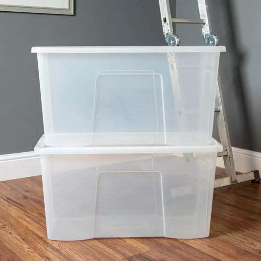 Three stacked Wham 110 litre clear plastic storage boxes with blue clip-on lids filled with blankets and clothes inside a brightly lit home closet.