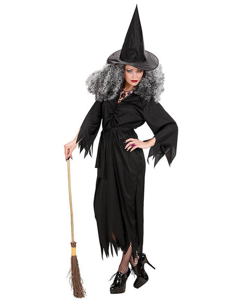 Adult wearing a black witch costume with a pointed hat and long flowing sleeves against a dark neutral background.