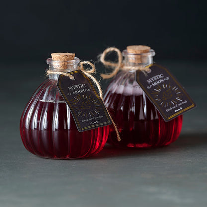 Pair of small clear glass Witch's Brew potion bottles with vintage distressed labels sitting on a dark wooden surface.