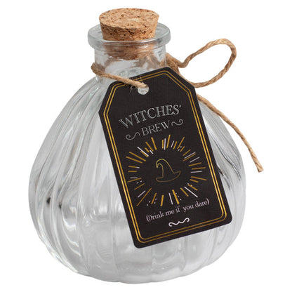 Pair of small clear glass Witch's Brew potion bottles with vintage distressed labels sitting on a dark wooden surface.