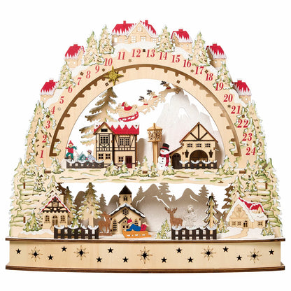 Front view of a laser-cut wooden alpine village advent calendar illuminated by warm internal LED lights on a wooden table.