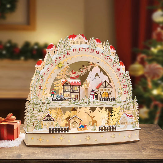 Front view of a laser-cut wooden alpine village advent calendar illuminated by warm internal LED lights on a wooden table.